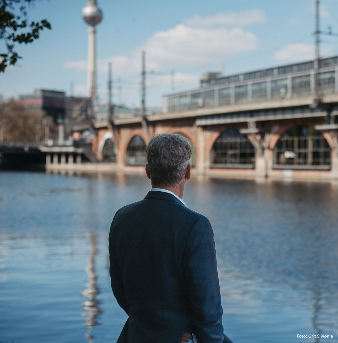Jochen Hummel seen from behind, looking across the river Spree towards the Berlin television tower and the railway viaduct